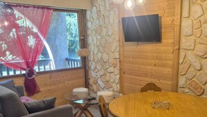 Ein gemütliches Zimmer mit Steinwand, einem Holztisch und einem an der Wand befestigten Fernseher.