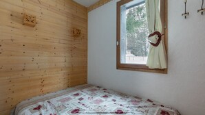 Ein Schlafzimmer mit Holzwandverkleidung, einem Einzelbett mit gemustertem Bettbezug, einem Fenster mit Vorhang und einer kleinen Holzdekoration an der Wand.