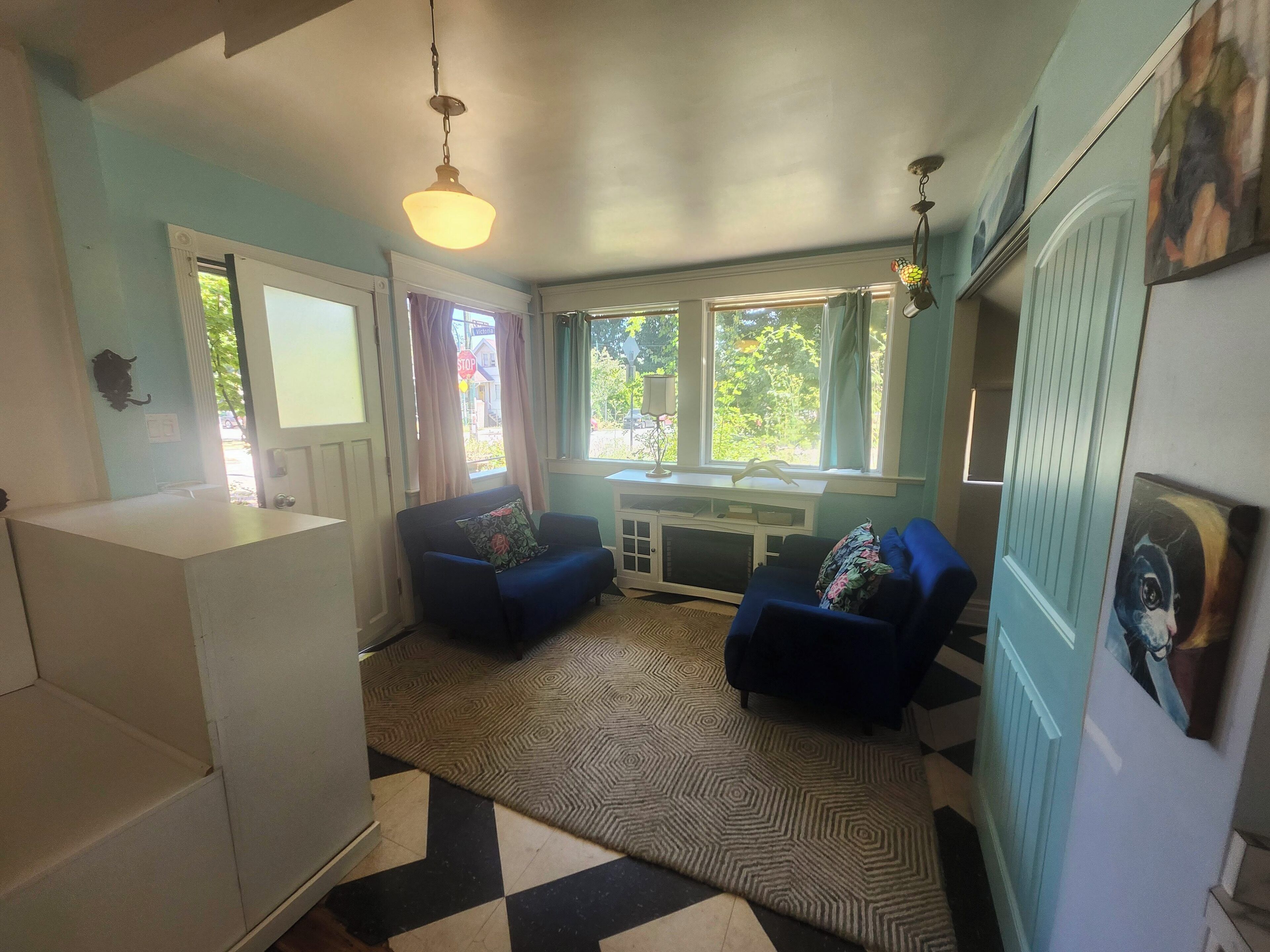 A compact living space with a kitchenette, two sofas, a patterned rug, and a window with curtains.