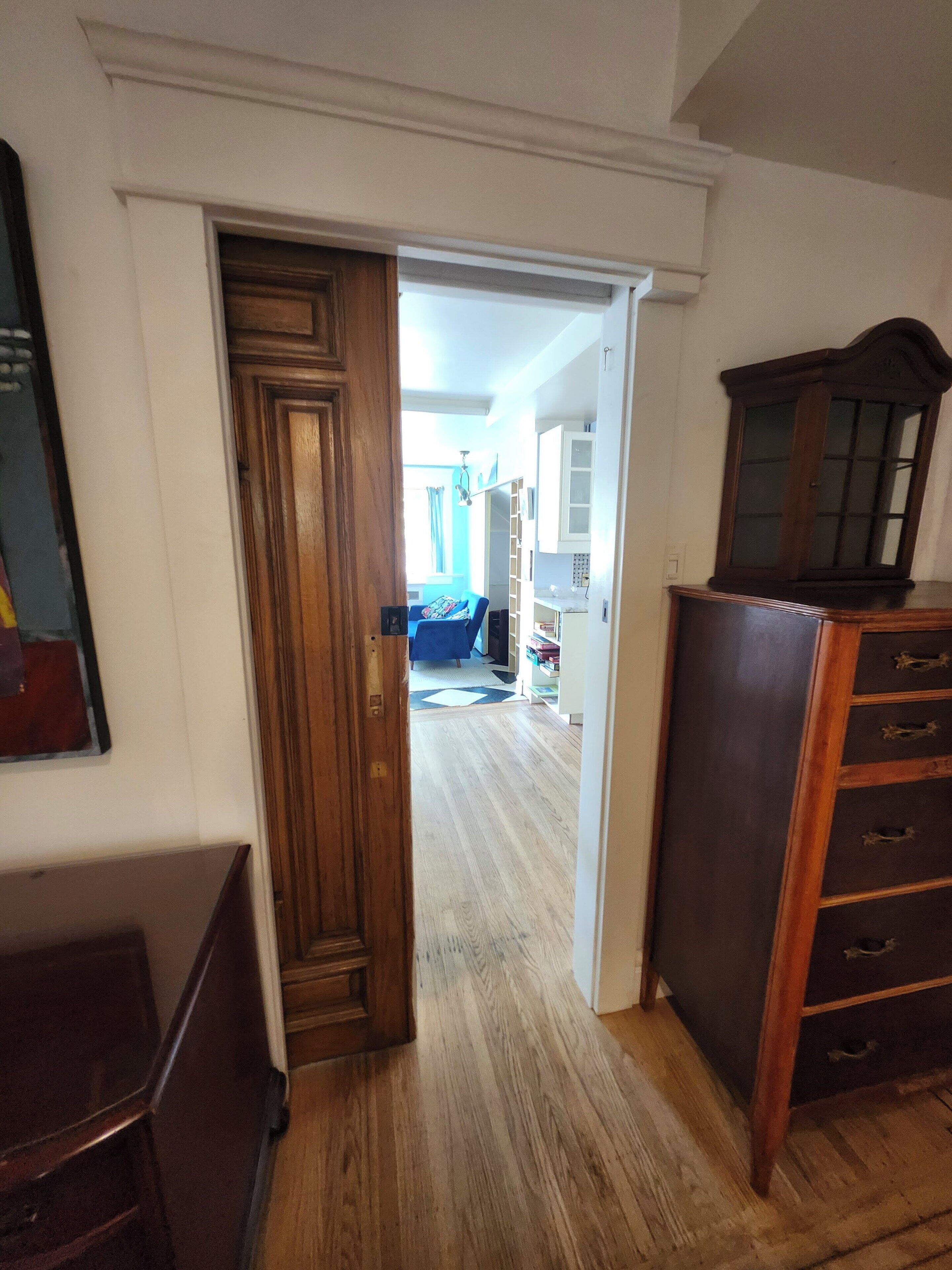 A hallway with a wooden door leading to a room with a blue sofa and a white cabinet.