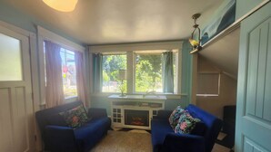 Une pièce avec deux fauteuils bleus, une cheminée blanche et une fenêtre avec des rideaux.