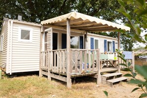 A mobile home with a wooden deck and a covered porch. - Bréhadour - Confort 3 TV - 7p (9) (Guérande)