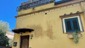 Un bâtiment jaune avec une porte en bois, un balcon doté d’une rambarde en métal et une fenêtre avec des volets verts.