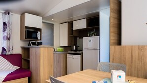 A compact kitchenette with a microwave, stove, and refrigerator. There is a dining table with chairs and a small seating area with a couch. - Bréhadour - Confort 4 TV - 9p (3) (Guérande)