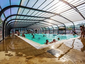 A covered swimming pool with a curved roof, surrounded by people swimming and lounging. - Bréhadour - Confort 4 TV - 9p (5) (Guérande)