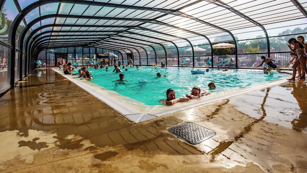 Une piscine couverte dotée d’un toit incurvé, entourée de personnes qui nagent et se détendent.