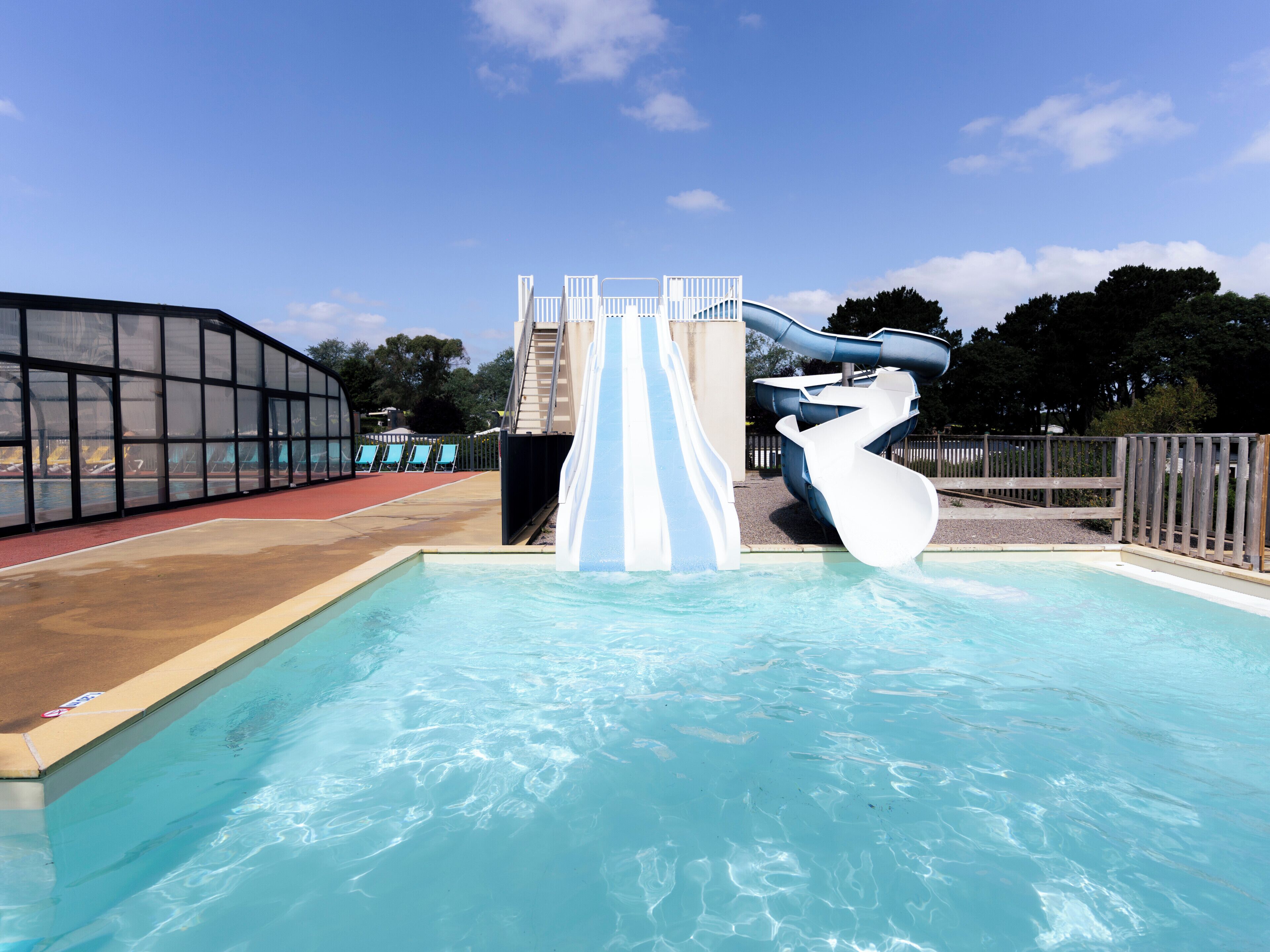 A swimming pool with a water slide and a covered area with chairs.