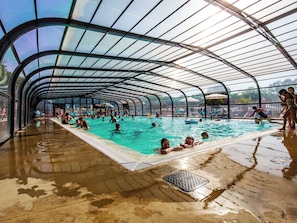 En inomhuspool med ett välvt tak, omgiven av folk som simmar och solar.