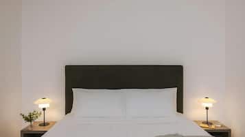Una cama bien hecha con sábanas blancas, un cabecero oscuro y dos mesitas de noche con lámparas.