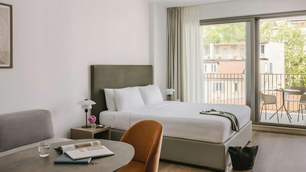 Ein Hotelzimmer mit Bett, Schreibtisch, Stuhl, Lampe und Blick ins Freie.