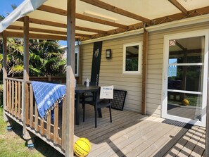 A covered outdoor area with a wooden deck, a table with chairs, a yellow ball, and a sign with text. - Gildas - Confort 2 TV - 5p (4) (Préfailles)