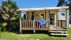 A small, single-story mobile home with a wooden deck, a covered porch, and a small window. - Gildas - Confort 2 TV - 5p (7) (Préfailles)