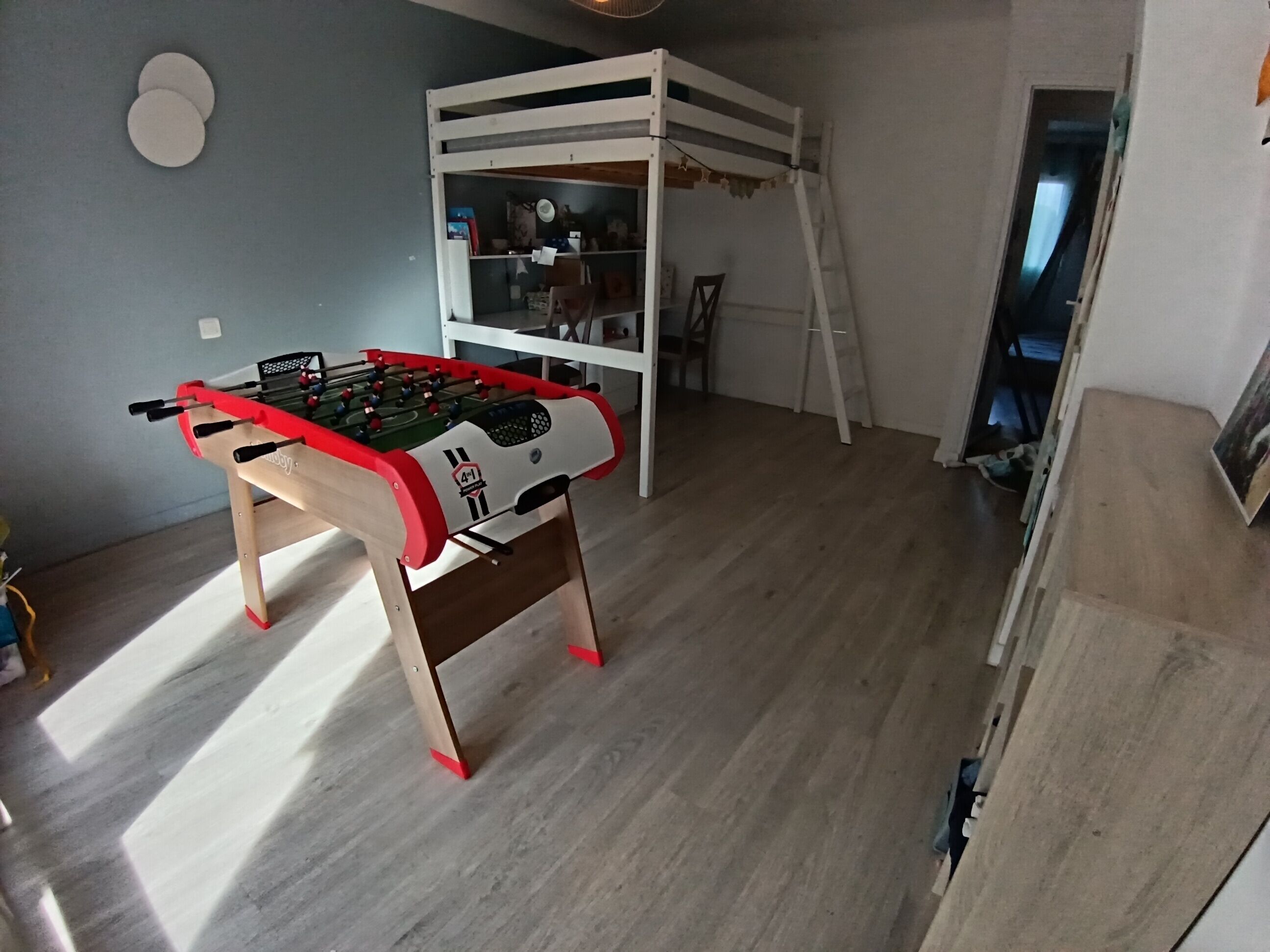 A room with a foosball table, a bunk bed, and a ladder.