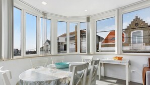 Habitación de esquina con ventanal saliente, una mesa de comedor con sillas y una mesita con una cesta.
