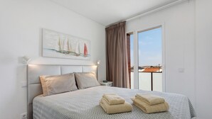 Un dormitorio con cama, almohadas, un cuadro, una mesita de noche y vistas a través de una ventana.