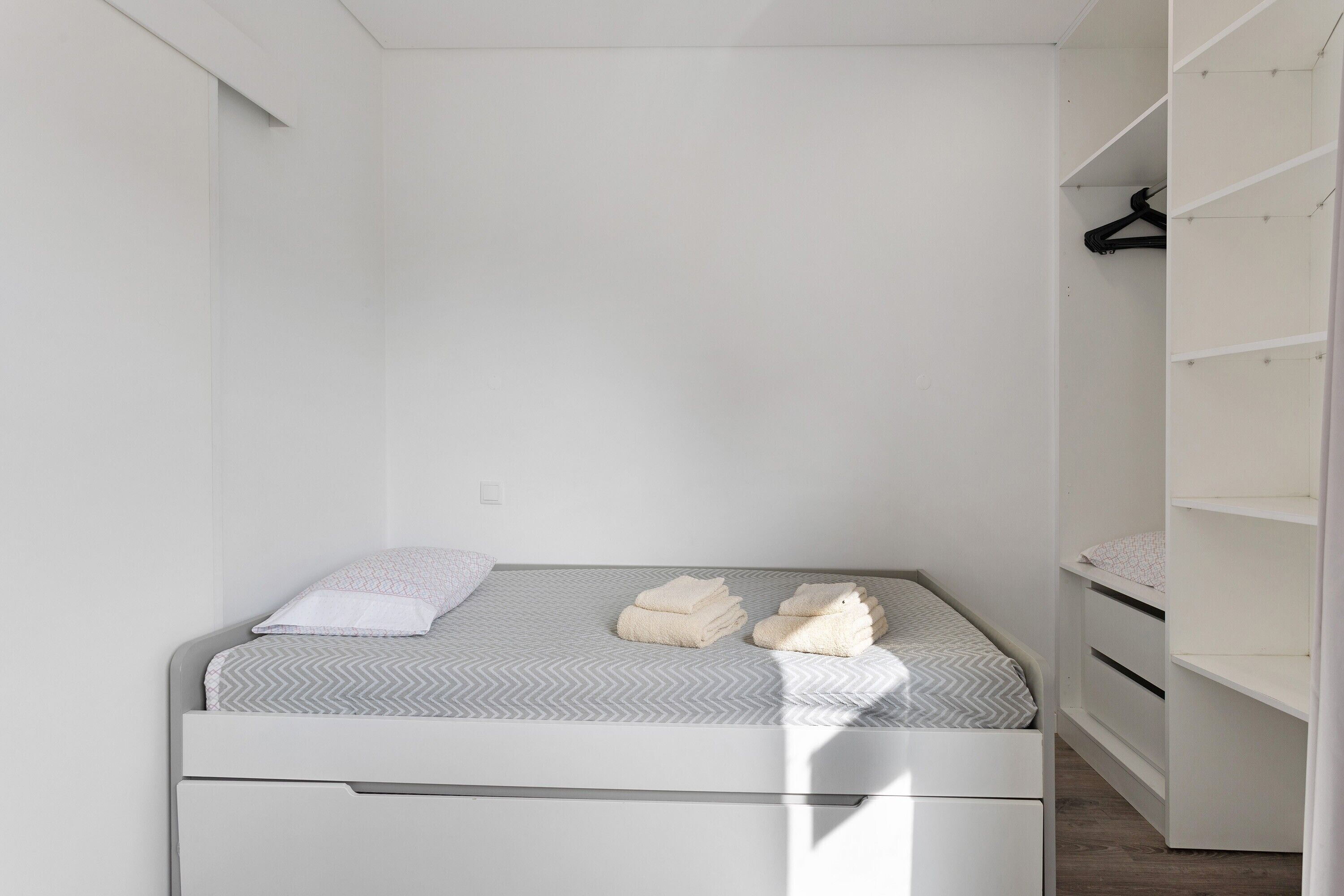 Ein schlicht eingerichtetes Schlafzimmer mit einem Bett, einem weißen Kleiderschrank und einer Kleiderstange.