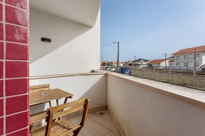 A balcony with a table and chairs, a red-tiled wall, and a view of parked cars and houses. - Apartment 'Dos Terraços T3 Rc' with Balcony, Wi-Fi and Air Conditioning (São Martinho do Porto)