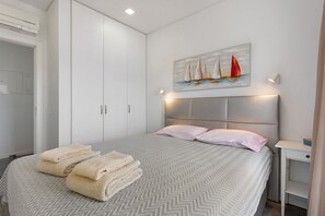 A bedroom with a bed, a headboard, a painting of sailboats, a bedside table, and a wardrobe. - Apartment 'Dos Terraços T3 Rc' with Balcony, Wi-Fi and Air Conditioning (São Martinho do Porto)