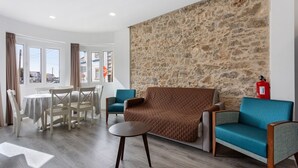Una habitación con pared de piedra, un sofá marrón, sillones color turquesa, una mesa redonda y un comedor con sillas y una mesa.