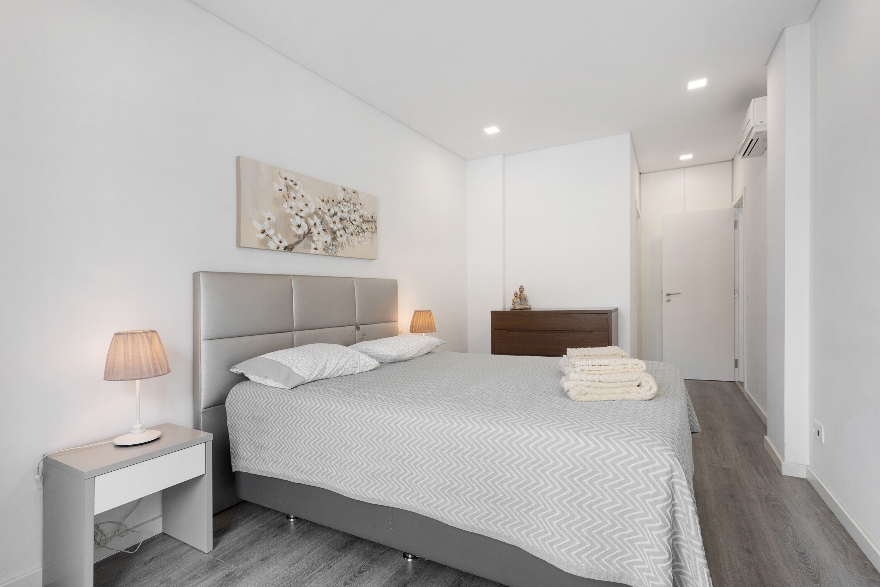 A modern bedroom with a bed, bedside table, lamp, artwork, and a wardrobe.