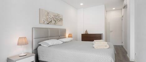 A modern bedroom with a bed, bedside table, lamp, artwork, and a wardrobe.