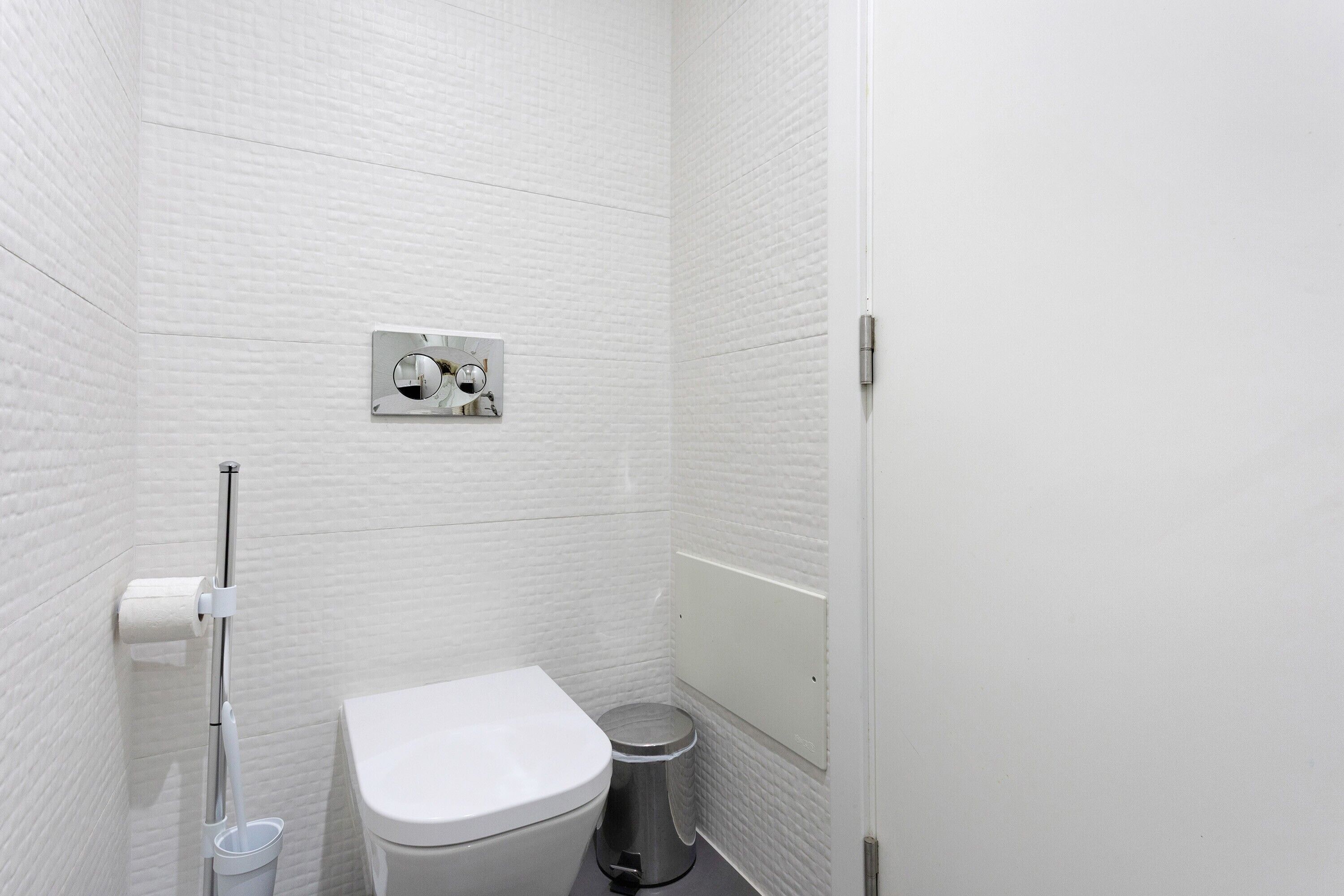 Une petite salle de bain aux murs blancs, équipée de toilettes, d’une poubelle et d’un distributeur d’essuie-tout.