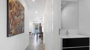 Un pasillo con un lavamanos moderno, una zona de comedor con sillas y un cuadro abstracto grande en la pared.