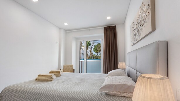 Una habitación de hotel moderna con una cama grande, una lámpara de noche, vistas al exterior y una ventana con cortinas.