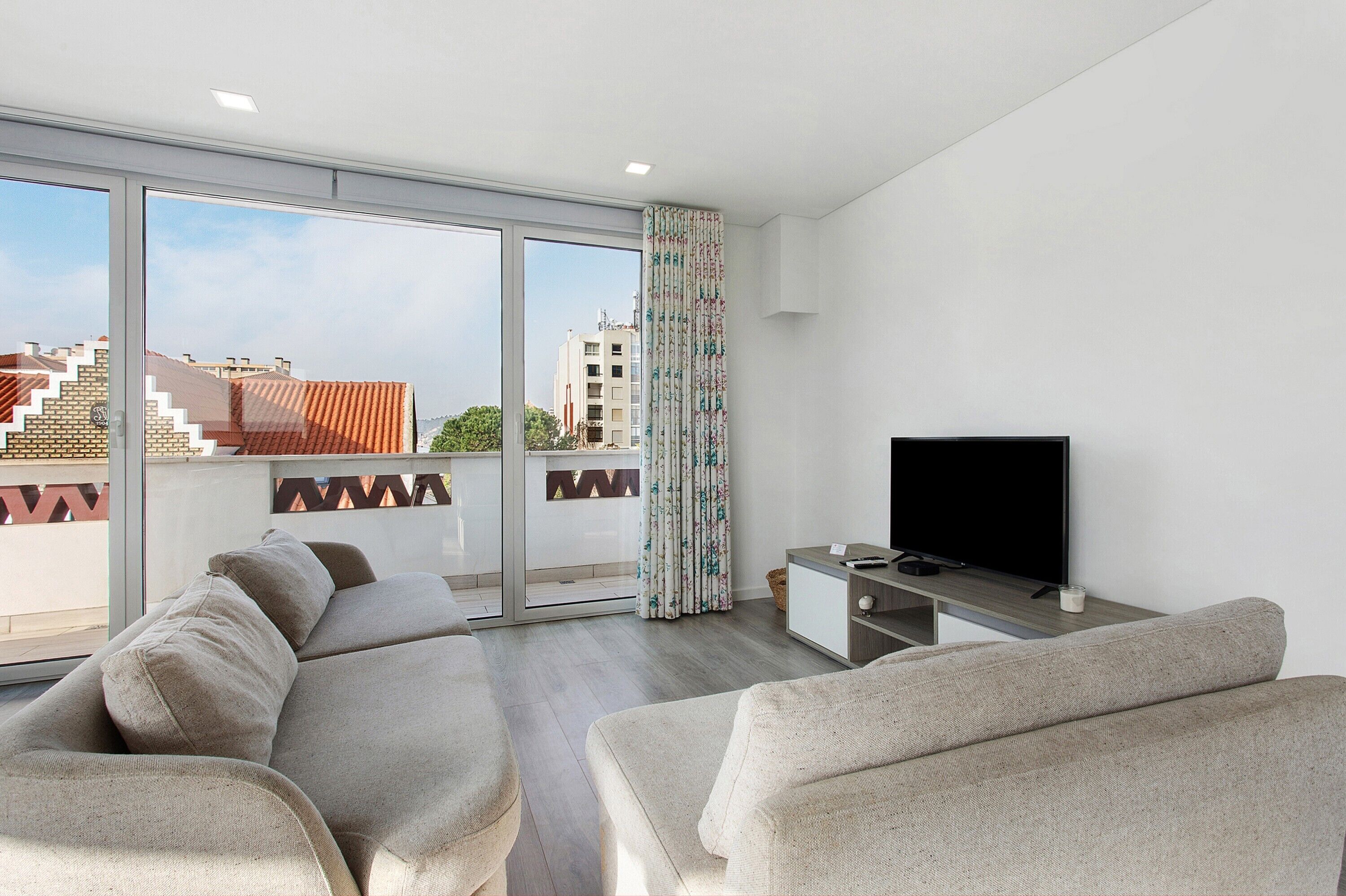 A modern living room with a large window, a flat-screen TV, and a sofa.
