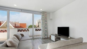 A modern living room with a large window, a flat-screen TV, and a sofa. - Apartment 'Casa Dos Terraços Penthouse' with Balcony, Wi-Fi and Air Conditioning (São Martinho do Porto)