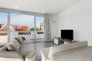 A modern living room with a large window, a flat-screen TV, and a sofa. - Apartment 'Casa Dos Terraços Penthouse' with Balcony, Wi-Fi and Air Conditioning (São Martinho do Porto)