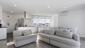 A modern living room with a grey sofa, a dining area with a white table and chairs, and a kitchen in the background. - Apartment 'Casa Dos Terraços Penthouse' with Balcony, Wi-Fi and Air Conditioning (São Martinho do Porto)