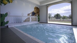 Een wellnessruimte met een jacuzzi, een decoratieve wand met cactussen en uitzicht door een glazen deur.