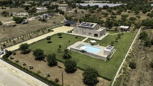 Luchtbeeld van een woonhuis met zwembad, zonnepanelen en een verzorgd gazon.
