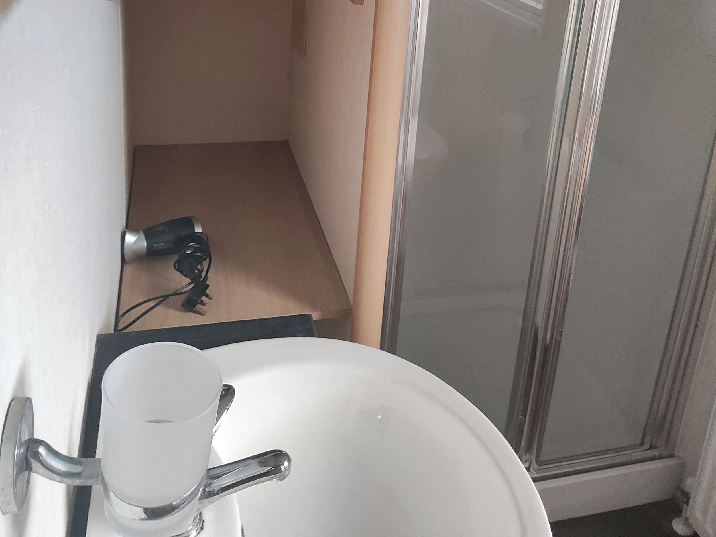 Et badeværelse med en hvid vask, et glas og en hårtørrer på gulvet.