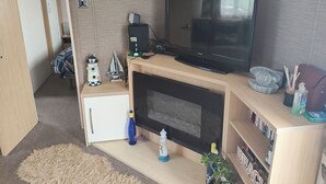 Un espacio habitable reducido con una televisión, un archivador pequeño, una estantería y un velero decorativo.