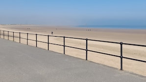Una playa con baranda metálica y cielo despejado.