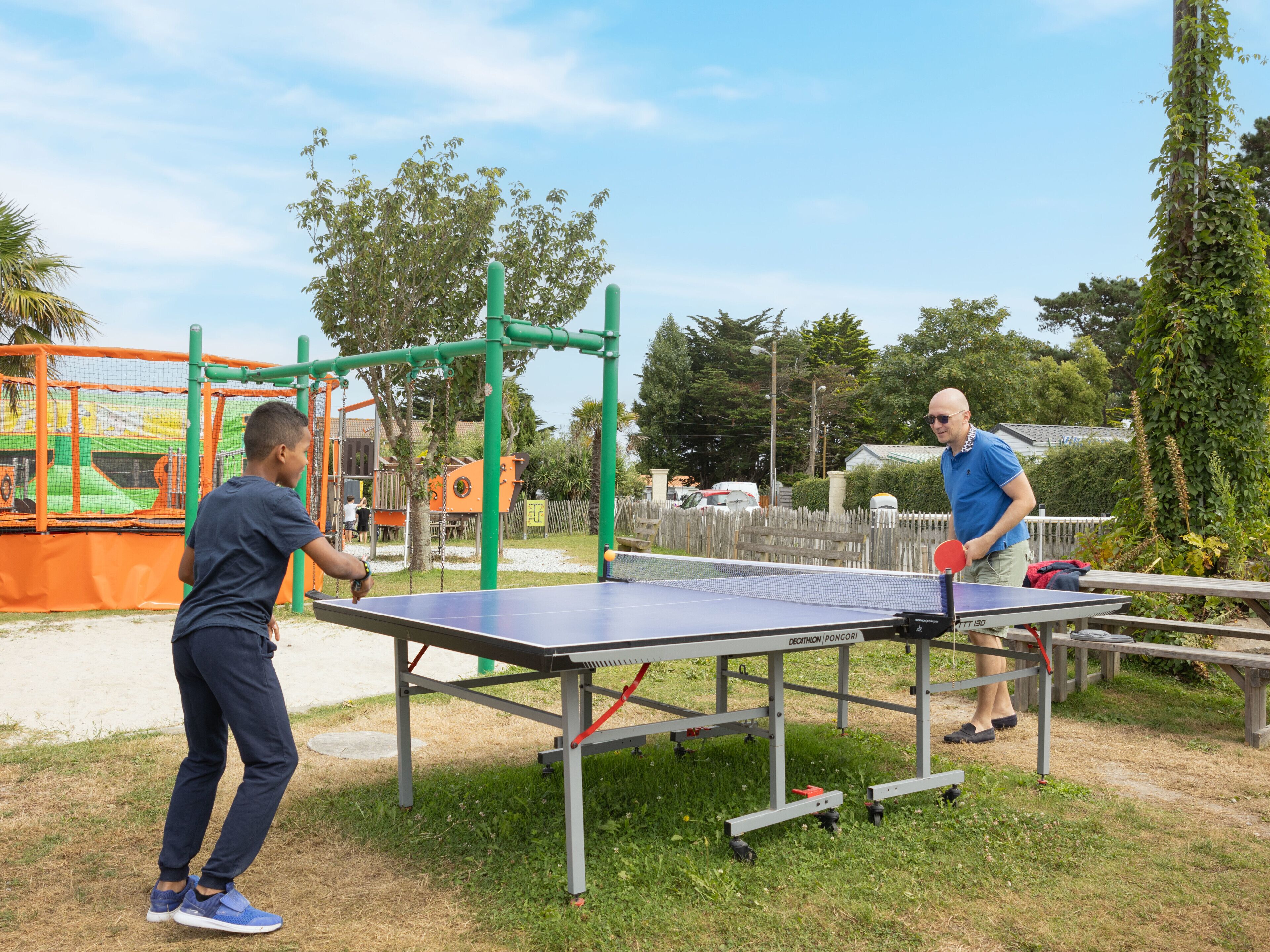 Dues persones jugant a tennis taula a l'aire lliure, amb una taula i una xarxa.