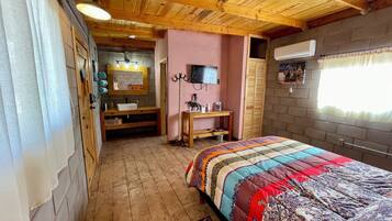 A bedroom with a wooden ceiling, a bed with a colorful quilt, a vanity with a mirror, and a television on the wall.