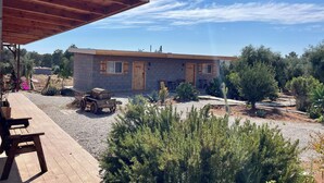 A small stone building with a wooden door and windows, surrounded by greenery and a gravel path. - Wine Country Retreat: Sleeps 8-Beautiful 4BR Cabin with A/C  Valle de Guadalupe (Ensenada)