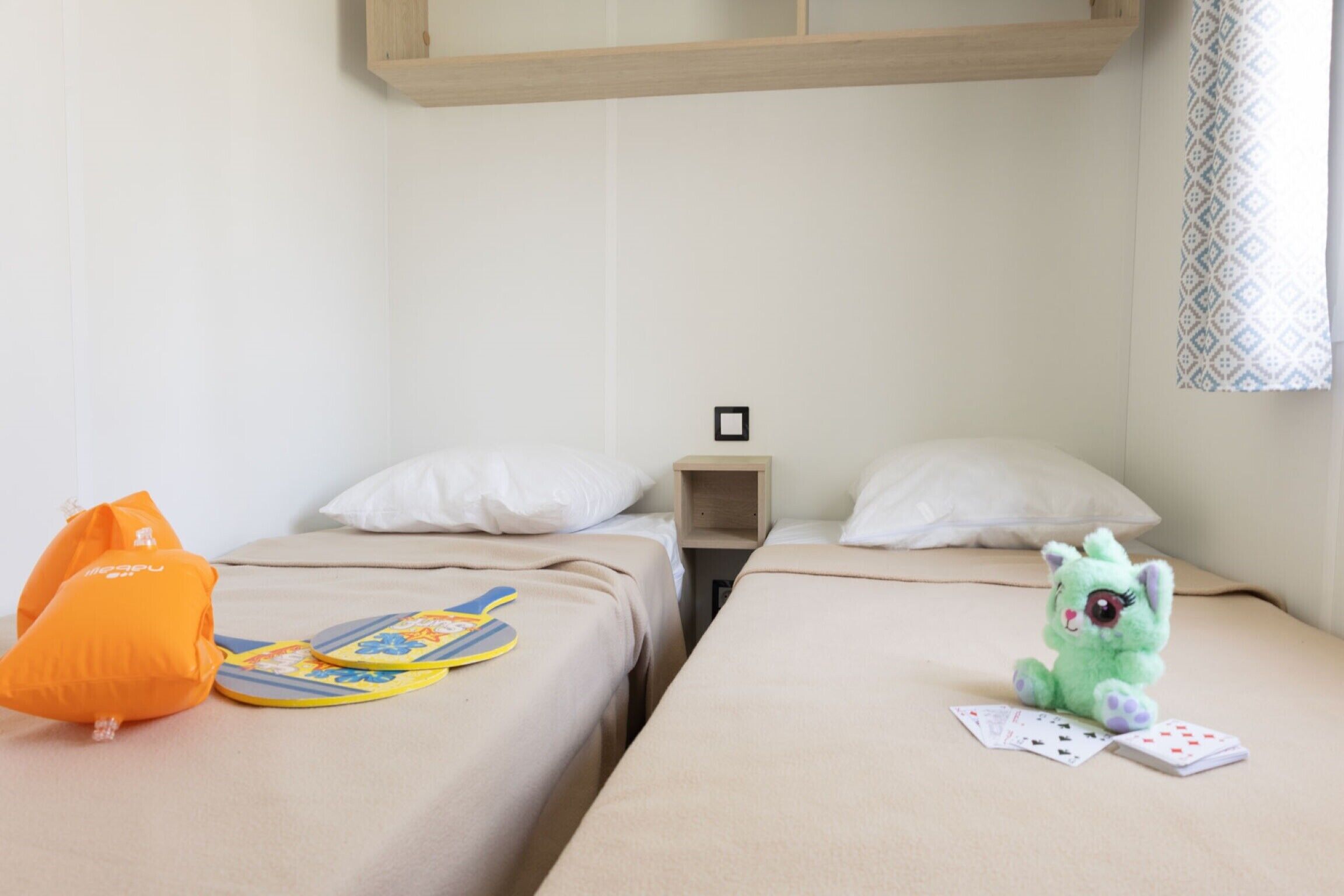 Habitación de hotel con dos camas, una mesita de noche, un peluche y un par de chanclas.