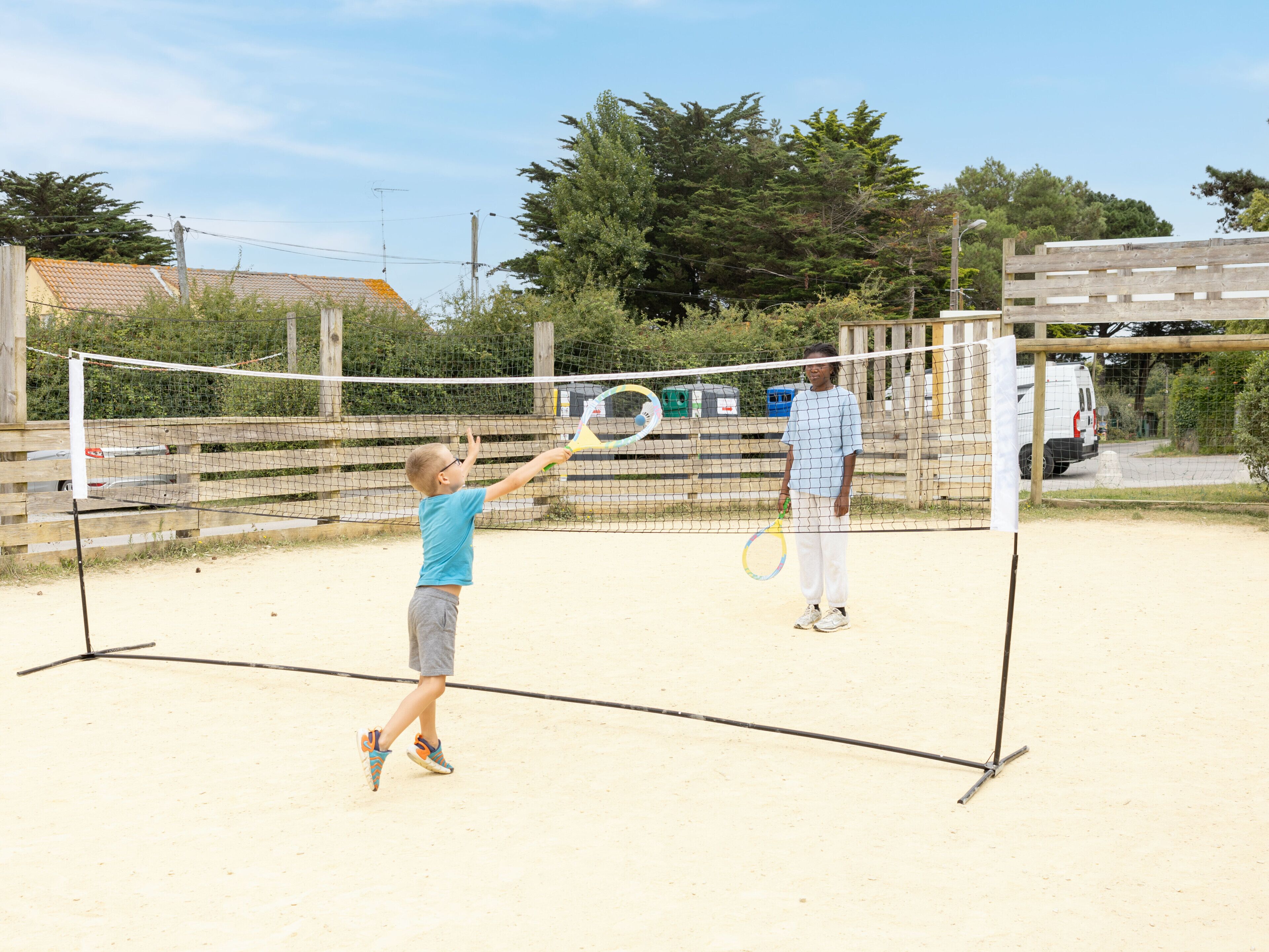 A tennis court with a net, a fence, and trees in the background.