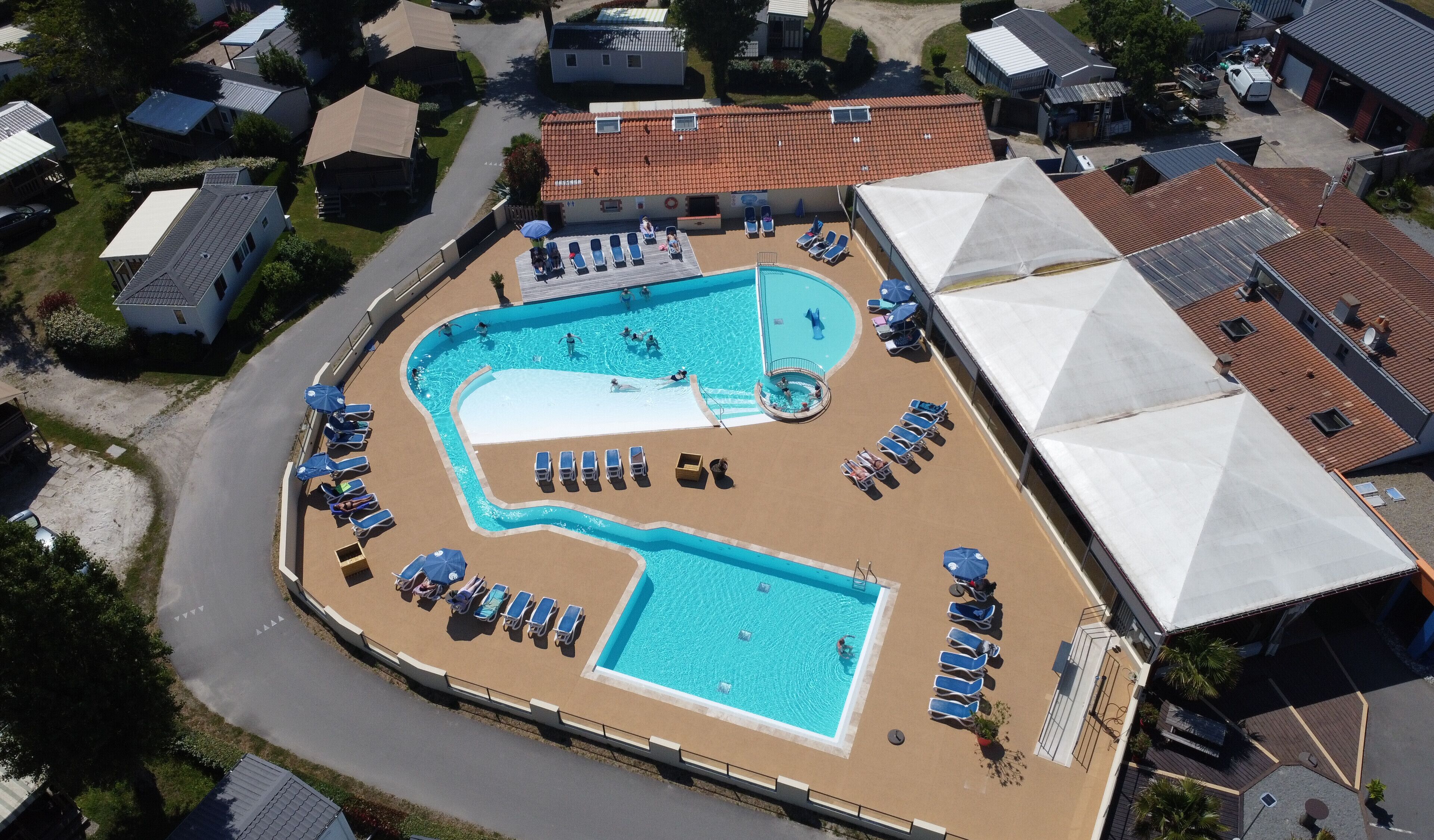 An aerial view of a residential area with a swimming pool surrounded by lounge chairs and umbrellas.