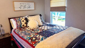 A bedroom with a large bed, a window with blinds, a decorative wall hanging, and a dresser. - Cozy 1-bedroom lake front cabin in the quaint town of Keystone Heights, FL (Keystone Heights)