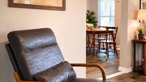 A leather armchair with wooden armrests in a room with wooden flooring, a dining area in the background, and a framed map on the wall. - Cozy 1-bedroom lake front cabin in the quaint town of Keystone Heights, FL (Keystone Heights)