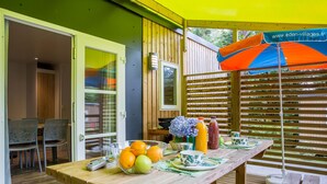 Een buitenterras met een houten tafel, gedekt met fruit, een schaal en een bloevas.