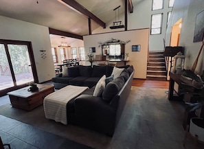 A spacious living room with a dark-colored sofa, a wooden coffee table, and a staircase leading to an upper level. - Cozy, peaceful mountain retreat in Lake Davis, Portola. Outdoor lover getaway! (Portola)