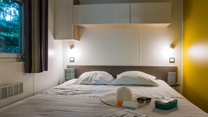 Ein ordentlich bezogenes Bett mit weißen Laken, Hut, Sonnenbrille und einer Zeitschrift.
