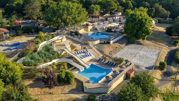 An aerial view of a resort with a swimming pool, lounge areas, and a covered deck. - Truffe - Chalet confort 2 – 5p (2) (Saint-Geniès)