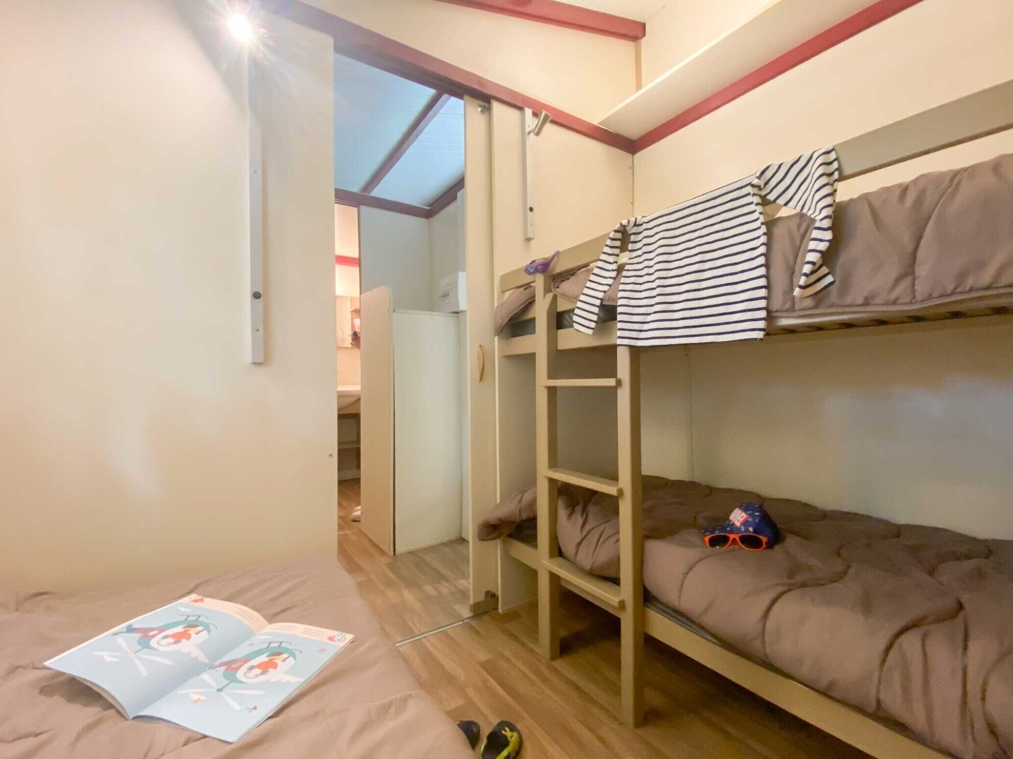 Une chambre avec un lit superposé, une échelle, une porte et un livre posé sur le sol.